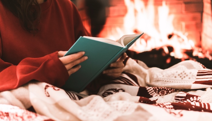 Girl reading book by clean cozy fireplace.