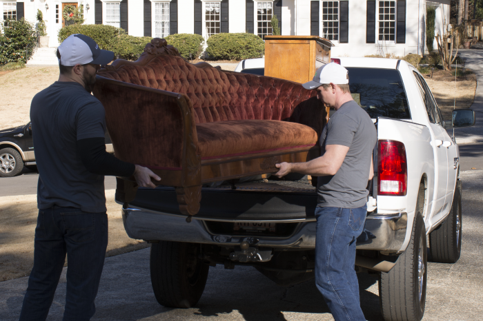 Two junk removal haulers loading an old couch into their truck