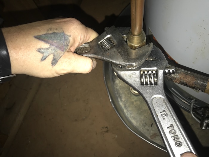 Hands using two wrenches to disconnect gas supply from hot water heater control valve