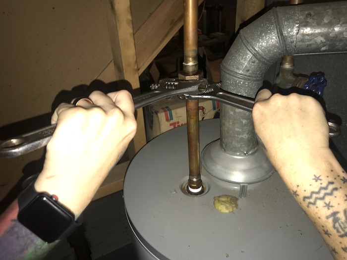 Two hands using two wrenches to disconnect hot water line from water heater