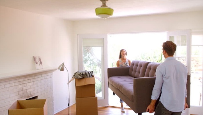 couple laughing carrying gray loveseat out of living room