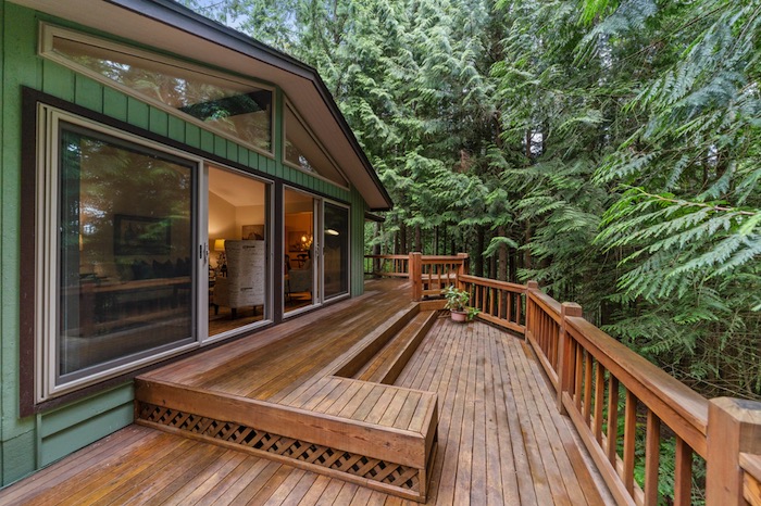 Big brown deck with green trees and a green home