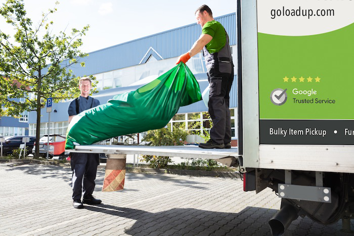 Two guys picking up a dumpster bag and loading it into a truck.