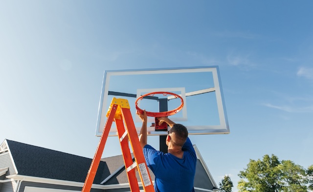 Guy on a ladder taking down an old basketball hoop for disposal.