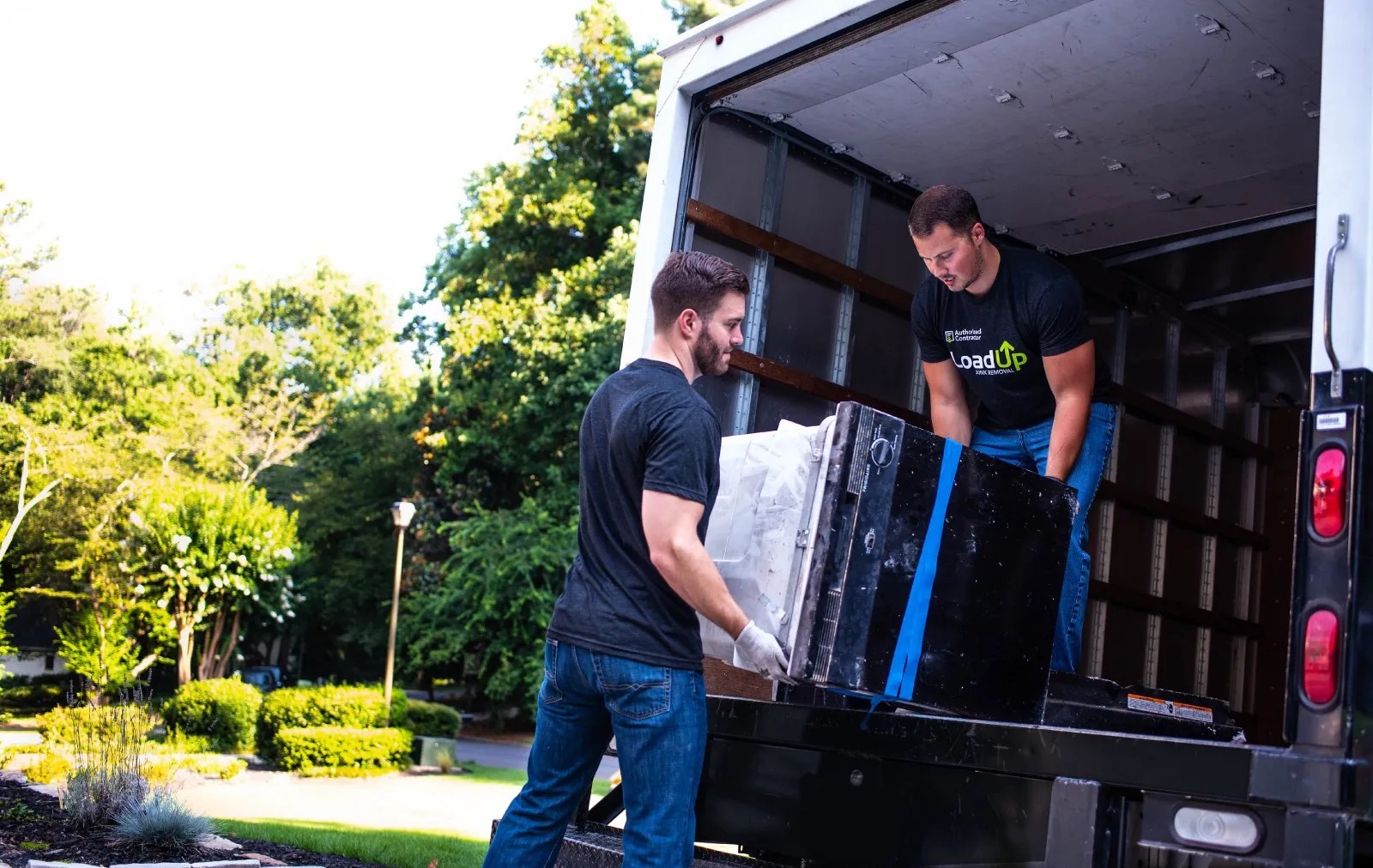 Two Loaders moving a dishwasher into the back of a truck for an estate cleanout.