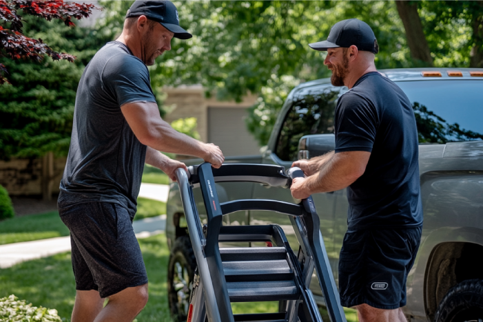 Two professional junk removal pros hauling away an old stair climber